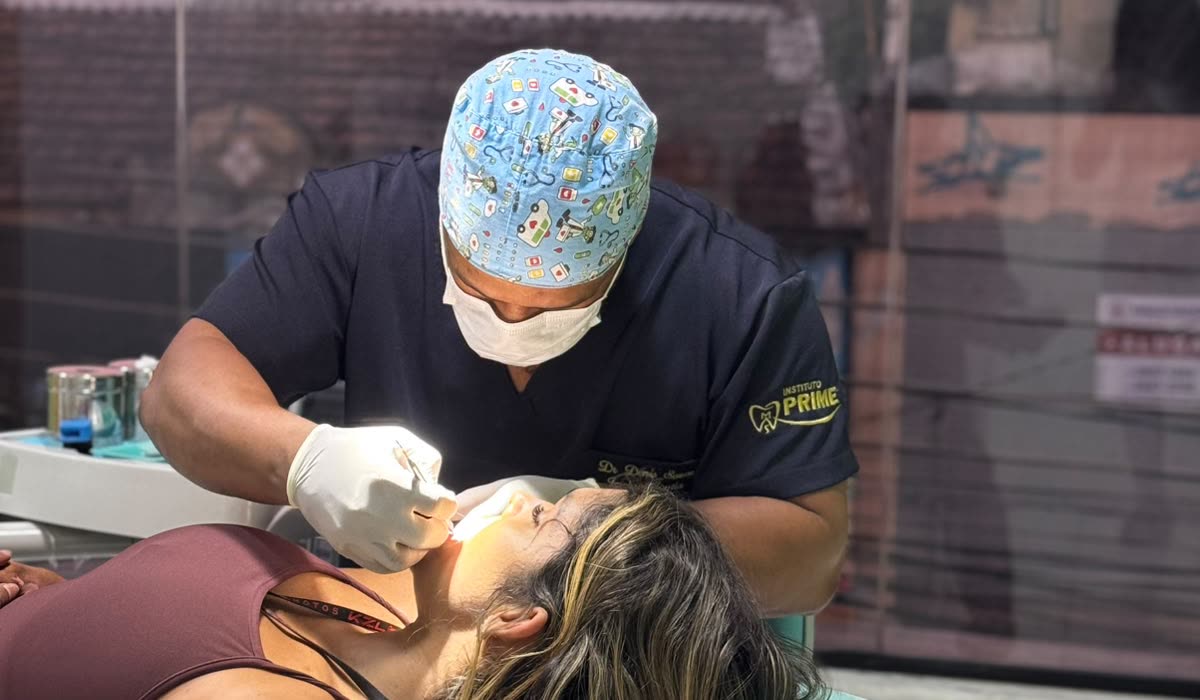 Dentista atende uma paciente na cadeira odontológica do consultório, com a janela ao fundo ao entardecer
